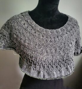 A gray, partially knitted "Panic Sweater" on a black dresss form.