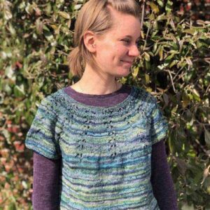 Young woman facing right wearing a knitted t-shirt in shades of blues, greens, and purples.